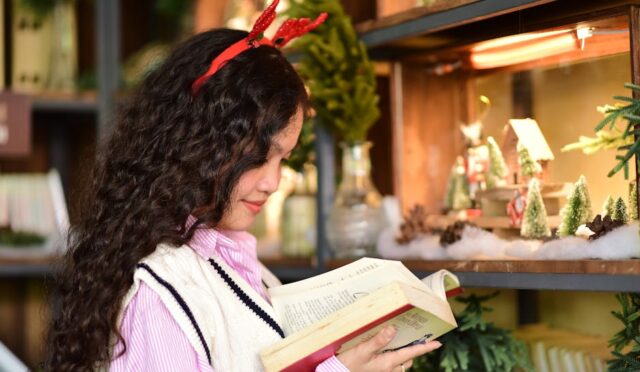 Noel başlığı takan bir kadın, iç mekanda kitap önerisi üzerine bir kitap okuyor.