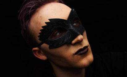 Siyah arka planda, kumral saçlı genç adam, makyajın sırları üzerine düşünceli bir şekilde bakıyor.