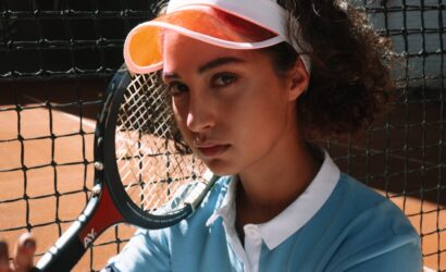 Genç kadın tenis oyuncusu, toprak kortta raketiyle tenis oynamak için hazır durumda.