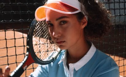 Genç kadın tenis oyuncusu, toprak kortta raketiyle tenis oynamak için hazır durumda.