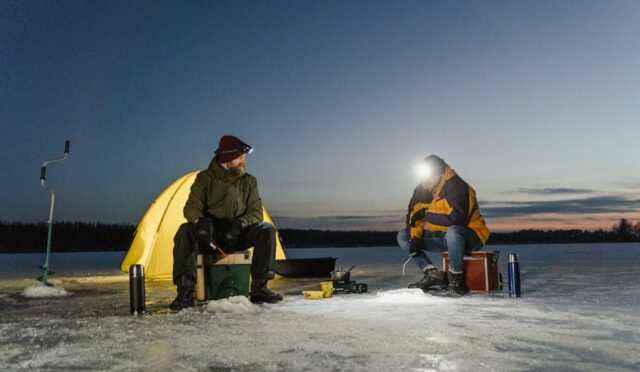 Karla kaplı gölde çadırın önünde balık tutmak için bekleyen iki adam, kış akşamı macerası yaşıyor.