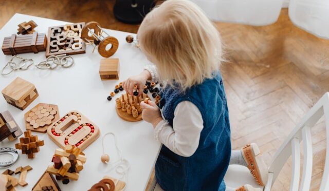 "Yüksek açıdan çekilmiş bu görselde, genç bir çocuk eğitim amaçlı ahşap oyuncaklarla puzzle oynuyor."